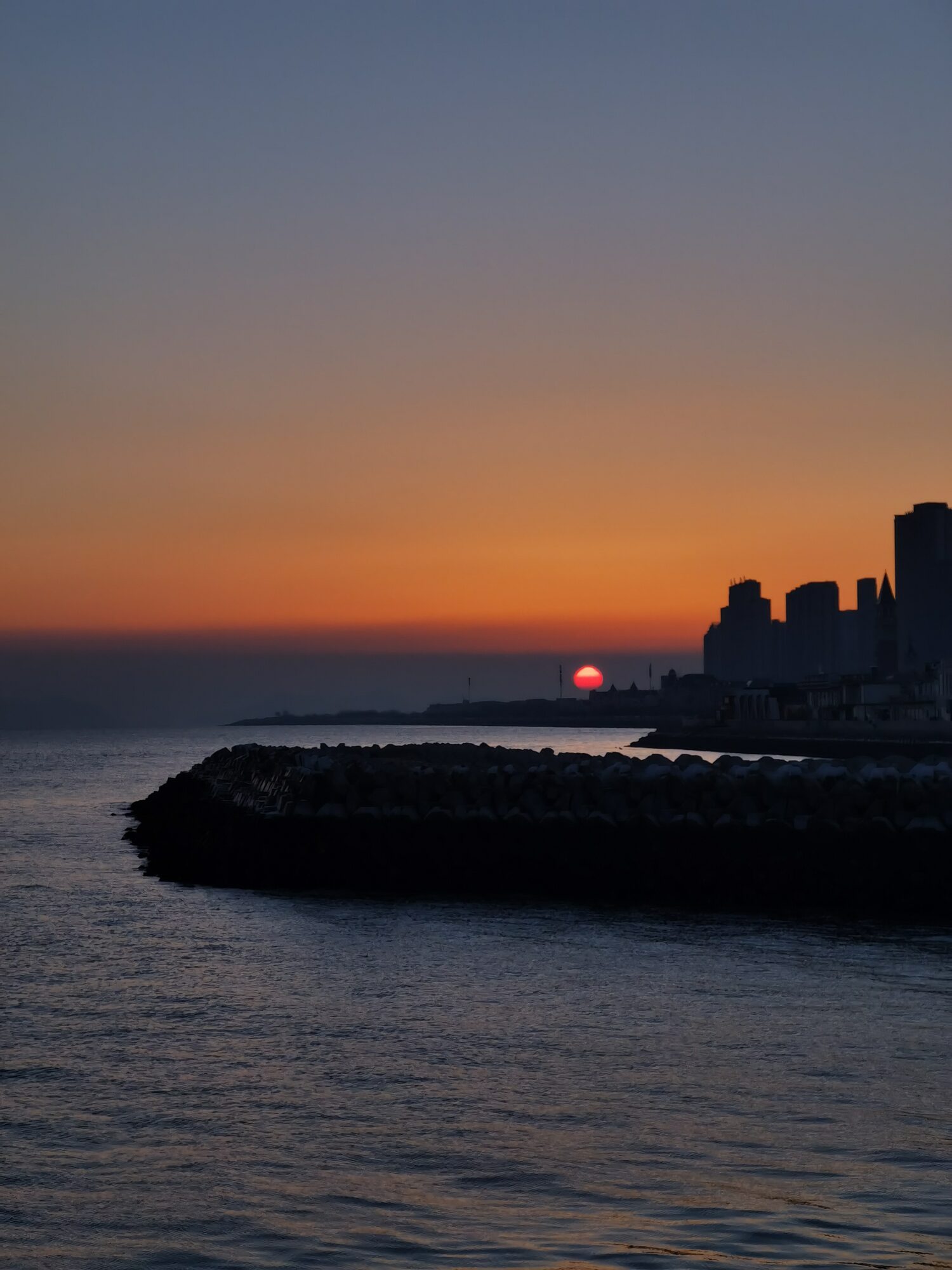 橙红色夕阳沉入海平面前的礁石