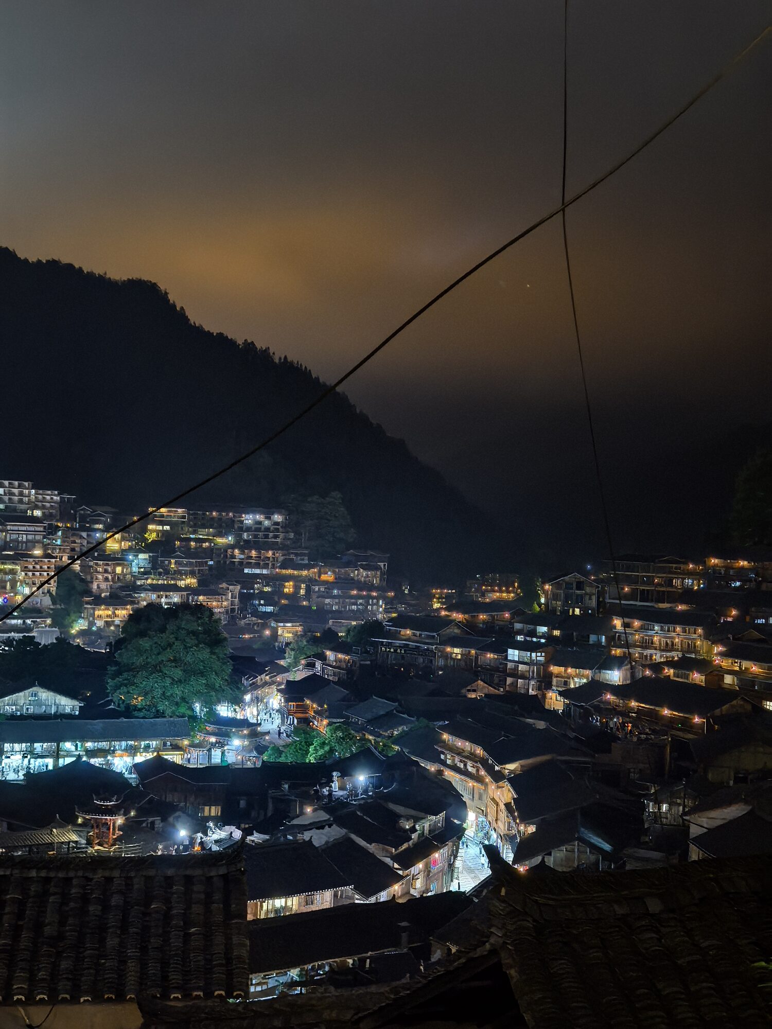 夜色中依山而建的古村落，木质建筑亮起层层灯光
